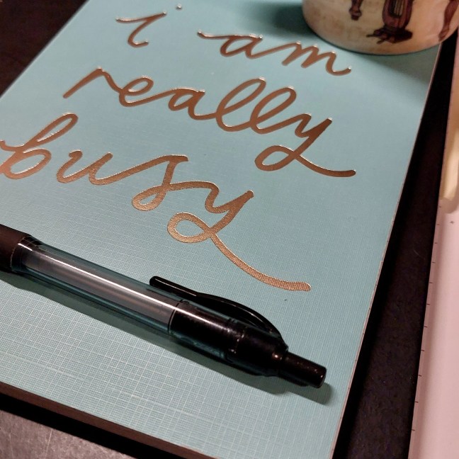Notebook cover reads, 'I am really busy'. Pen lying on the notebook.
