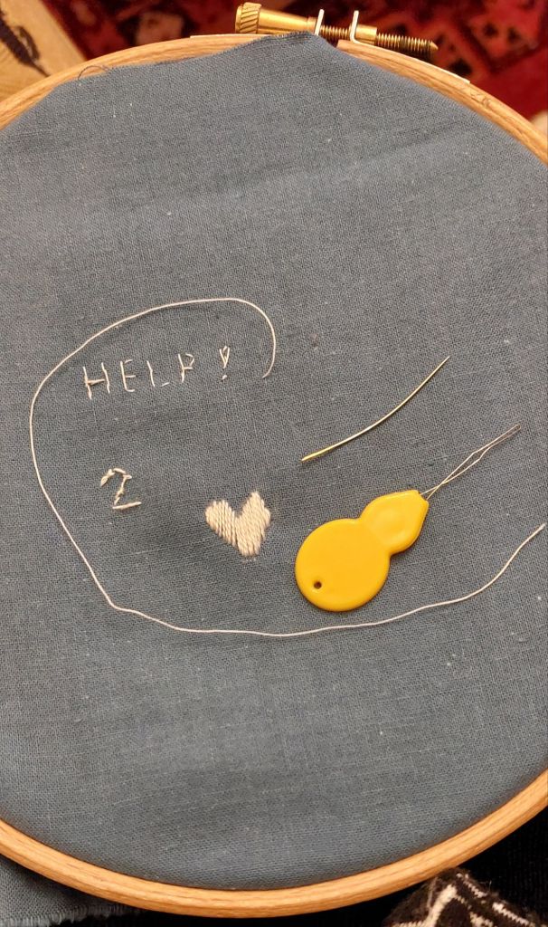 Embroidered word, HELP, a needle threader, a bent needle and an embroidered heart