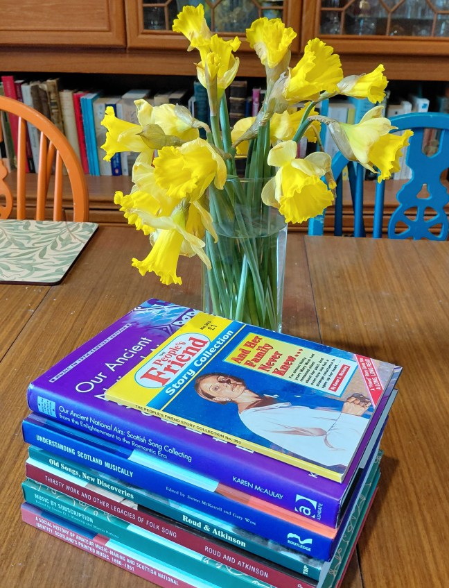 My two monographs, four contributed chapters, and a People's Friend paperback, on the dining room table, with a vase of daffodils.
