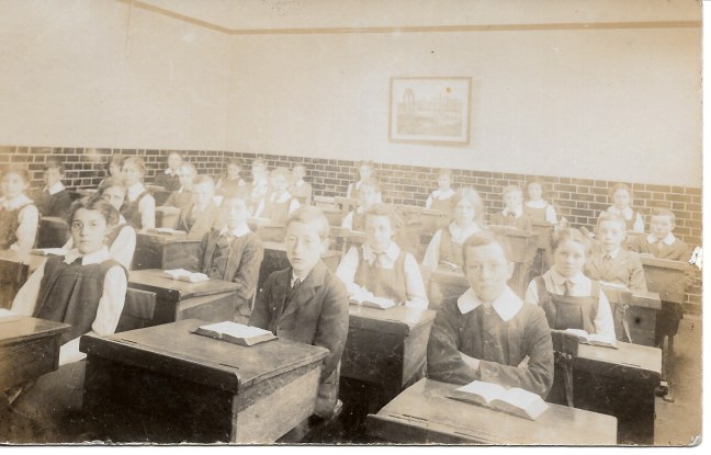 Faded old sepia photo of solemn children (Edwardian?) in a classroom