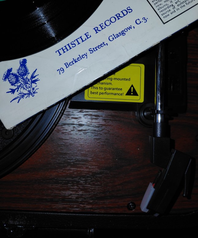 The Thistle Record label on a 45 rpm record cover, with the edge of a 45 rpm vinyl record, and a record turntable